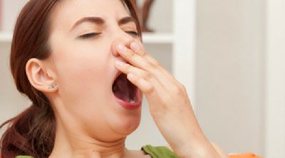 Overcome Exhaustion: Tips for Better Sleep. Tired woman sitting on the couch yawning.