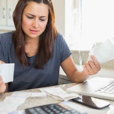 Simple Ways to Reduce Stress Over Money. Woman sitting at table with computer looking at bills.