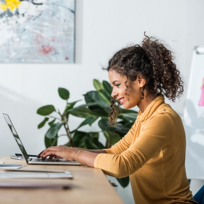 Steps to Promote a Wellness Workshop - Whole Family Living. Woman sitting at a desk typing on a laptop.