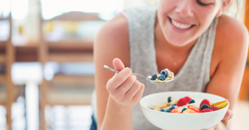 Happy woman haivng a healthy oatmeal berry breakfast bowl. Wellness Challenges to Improve Your Health - Whole Family Living