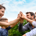 Family at the park, high-fiving while playing sports together. How to Plan a Family Wellness Challenge - Whole Family Living.